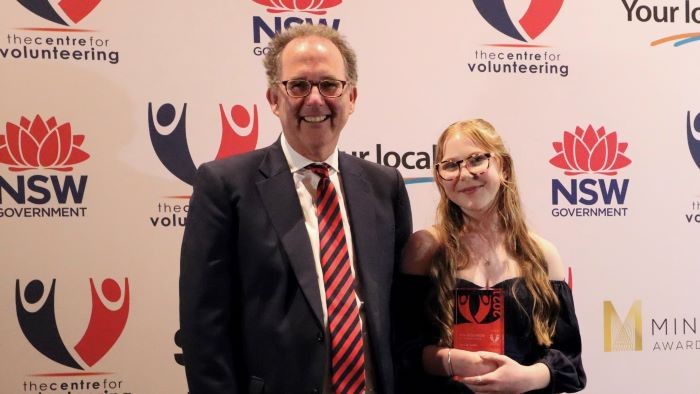 An older man stands next to a young woman who has received an award.
