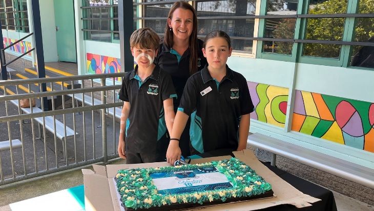 Two students and a teacher cutting a cake.