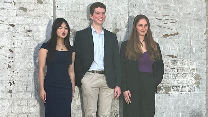 Three students standing in front of a white brick wall.