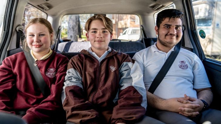 Three students wearing seatbelts sitting in the back of a van.