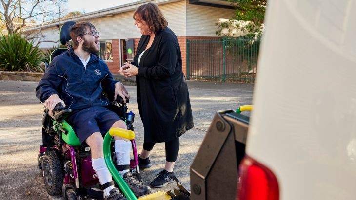 A student in a wheelchair with a lady beside a van.