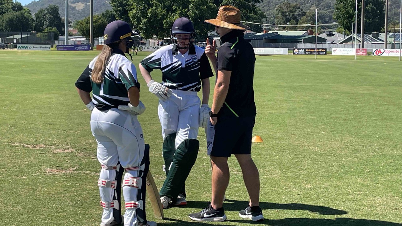 Two female cricketers and their coach discussing tactics