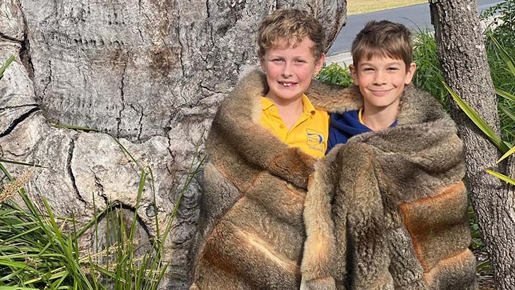 Two boys wearing a possum skin cloak.