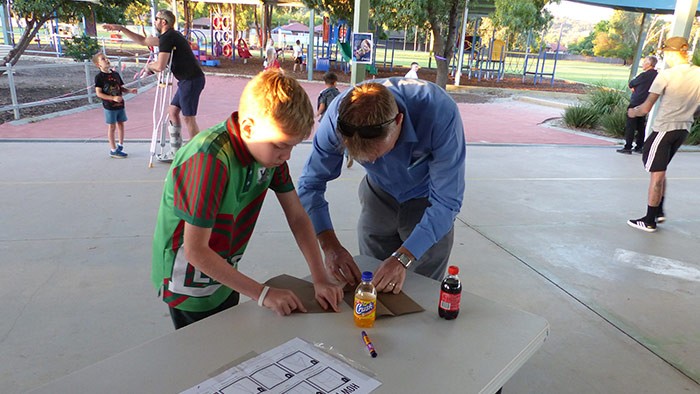 A boy and his father work together at a table building a paper plane