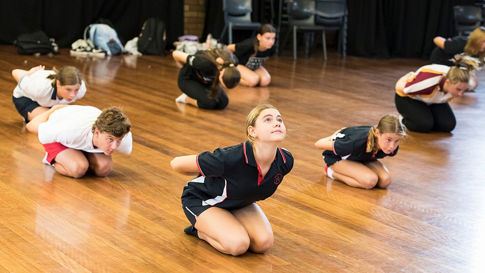 School students crouching on the floor as part of a dance routine.