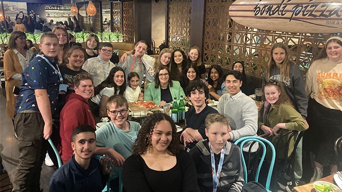 A group of students gather around one adult at a pizza restaurant