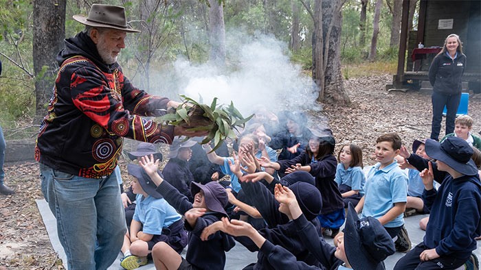 An Aboriginal elder doing a smoking ceremony while seated children look on