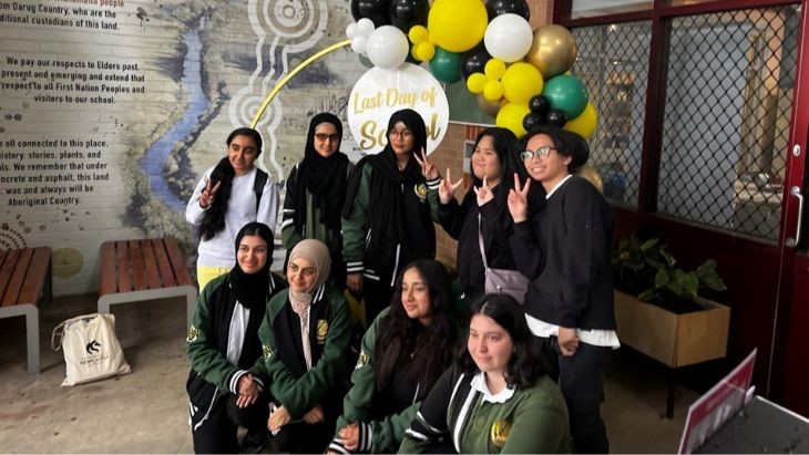 Students standing and sitting in front of coloured balloons.