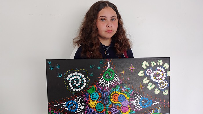 Student holds up colourful Aboriginal artwork