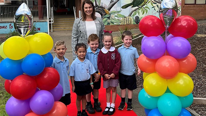 A teacher with five ilttle children standing on a red carpet surrounded by balloons