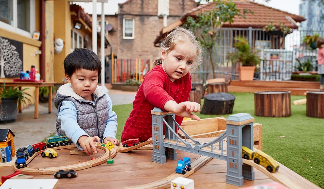 Two preschool children playing with a toy train set outside.