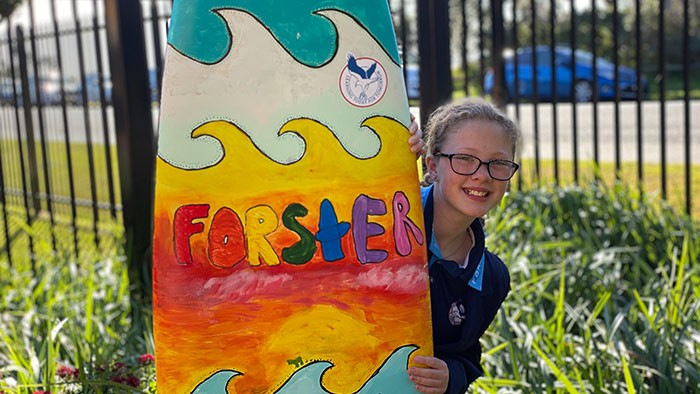 A young girl stands behind a brightly painted surfboard.