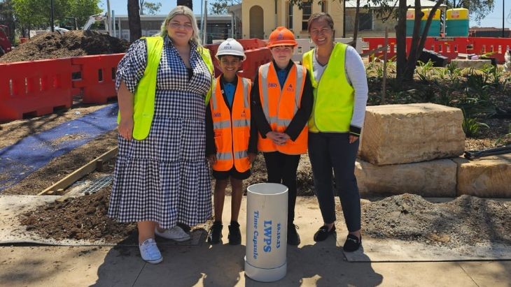 Two teachers with two students wearing high vis standing in front of a construction area.