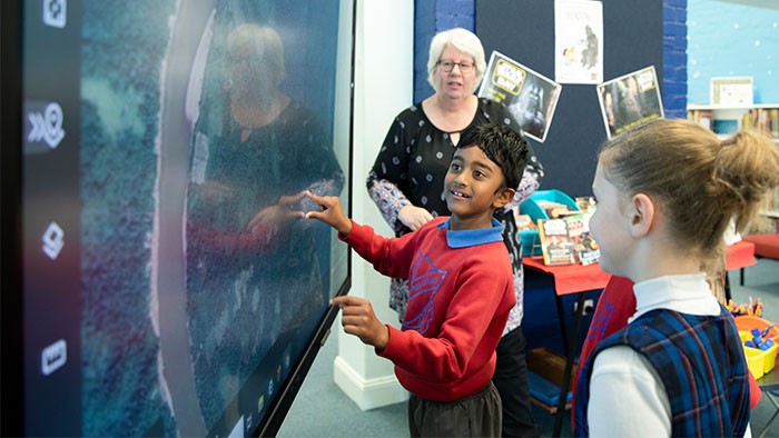 A young boy stands in front of a large interactive whiteboard