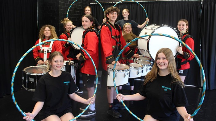 A group of musicians and dancers stand togethre holding instruments and hula hoops