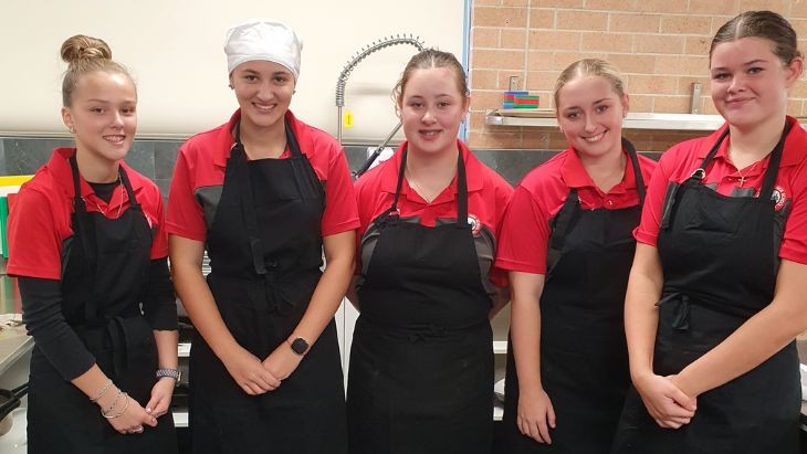 Five students wearing aprons.