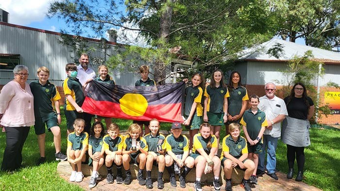 A group of students holding the Aboriginal flag standing with four adults
