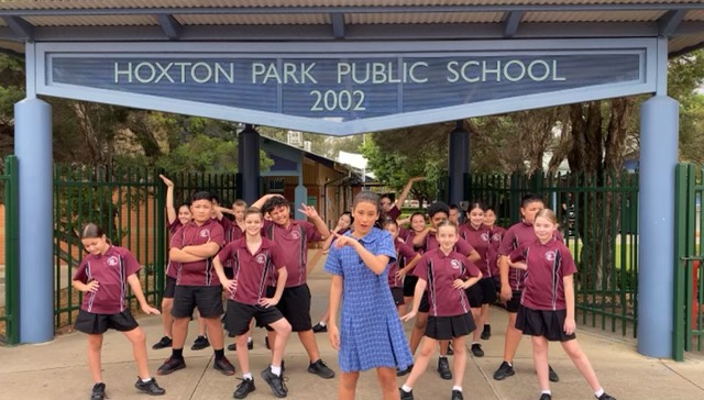 Group of students stand in front of school gate with Hoxton Park Public School 2002 sign above them