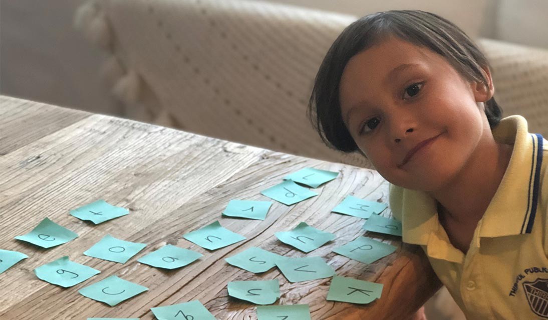 A boy smiling next to letter flash cards.