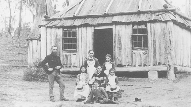 A family outside an old wooden hut.