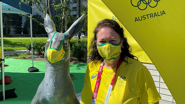 A woman wearing a face mask stands next to a kangaroo sculpture that is also masked up.