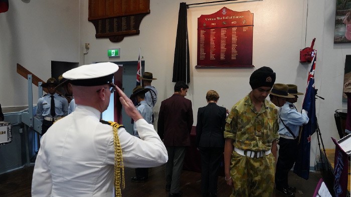 A serviceman saluting in front of an honour board