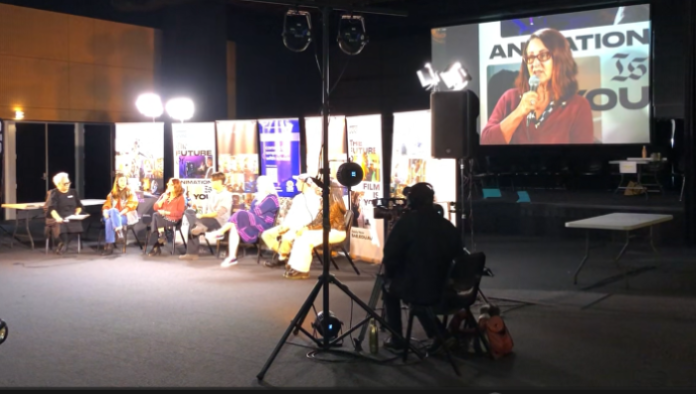 People in  panel sitting on chairs in front of television cameras