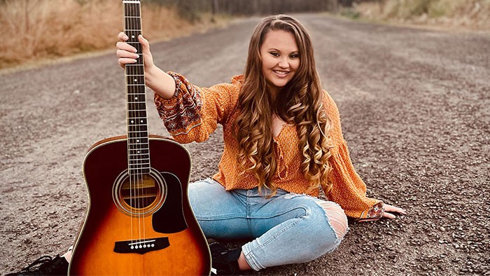 A young woman sitting on a country road holding a guitar