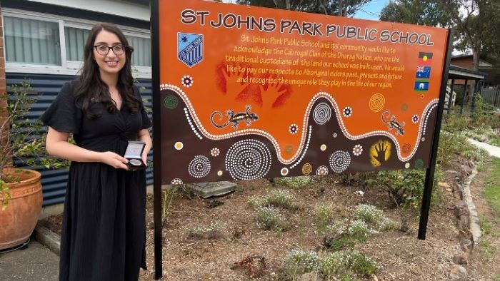 Kindergarten teacher holding medal and standing beside school sign