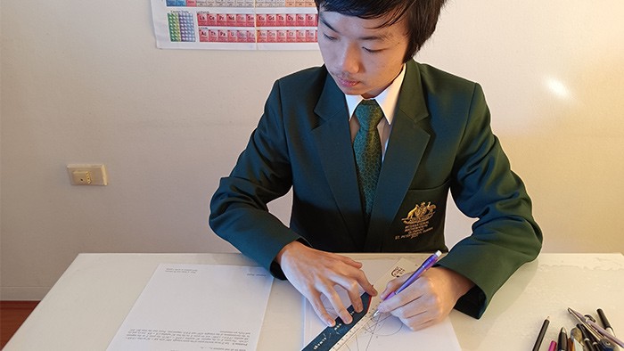 A young man in a suit sits at a desk doing mathematical work.
