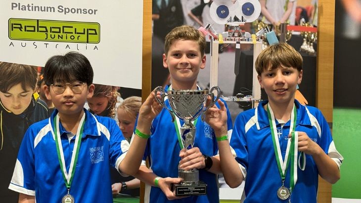 Students wearing medals and holding a trophy.