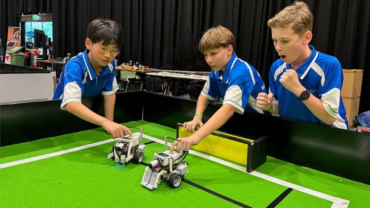 Students playing with Lego robots on a mini soccer field.