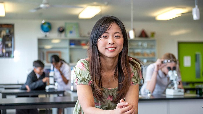 A young Asian woman with students at science benches in the background