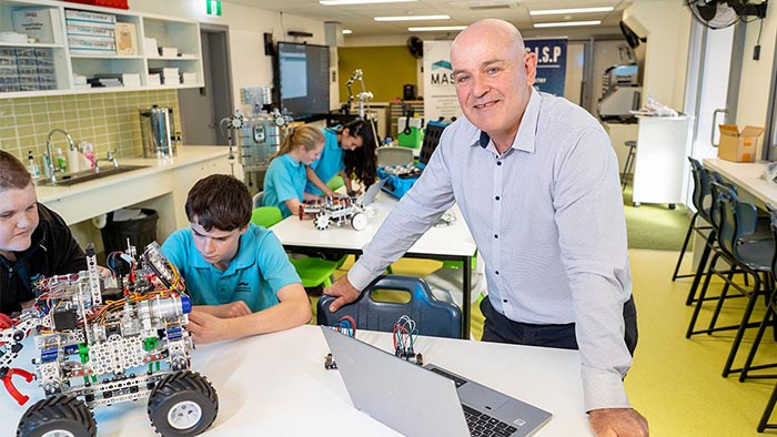 A male teacher at a desk with two students and a lego robot