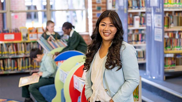 A long-haired Asian woman standing with a library and students in the background