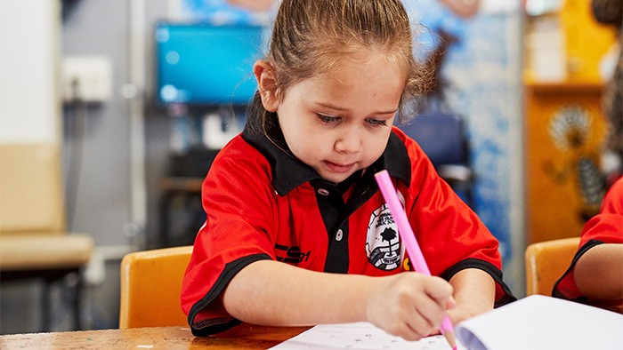 A young student holds a pink pen and is writing