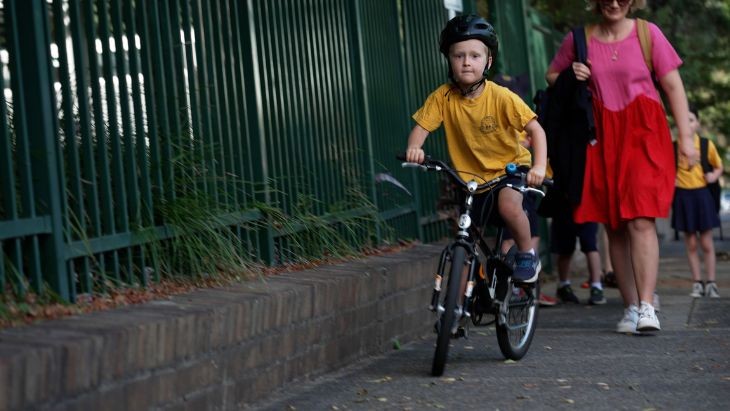A young male student riding a bike along a footpath.