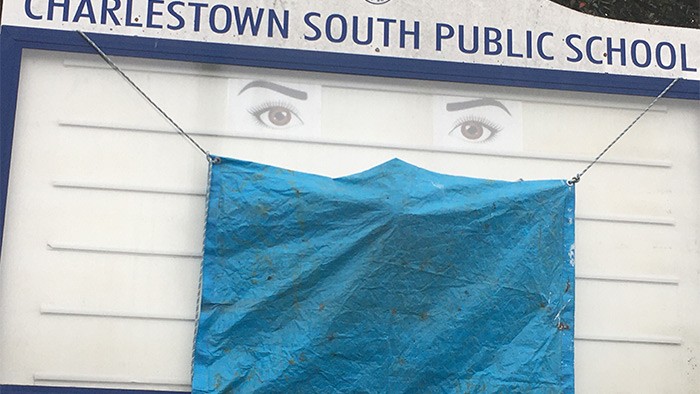 A school sign which has been altered to look like a face wearing a mask.