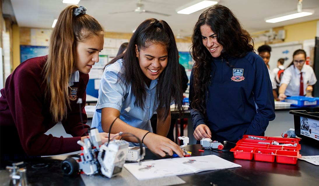 Three female high school students work on a robotics project.