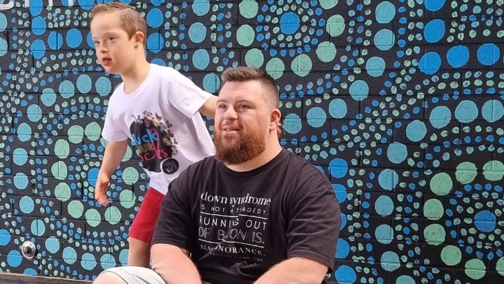 A boy and a man in front of an Aboriginal art mural on a wall.
