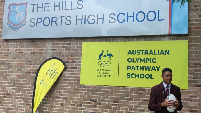 A boy holding a ball in front of some school and Olympic signage.