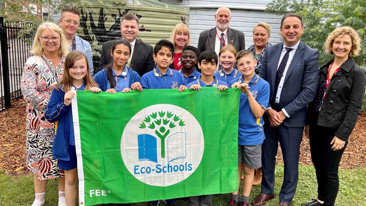Adults and children standing outside holding green environment award flag