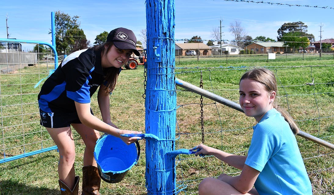 Two students painting a fence post blue.