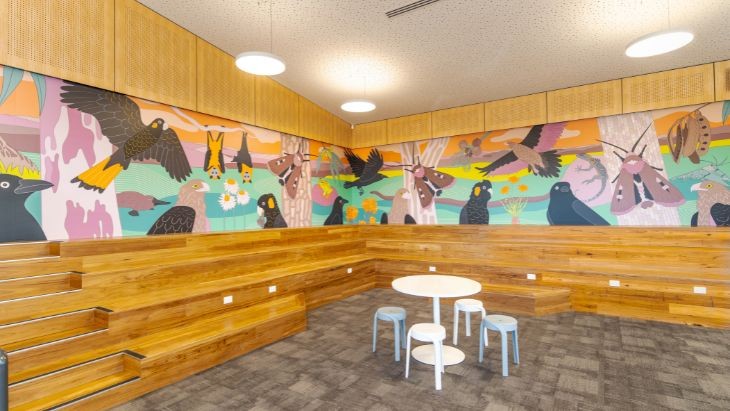 An empty classroom with a colourful wall mural of native animals including eagles, bats, moths and black cockatoos.