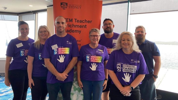 Teachers wearing purple shirts standing in front of a banner.