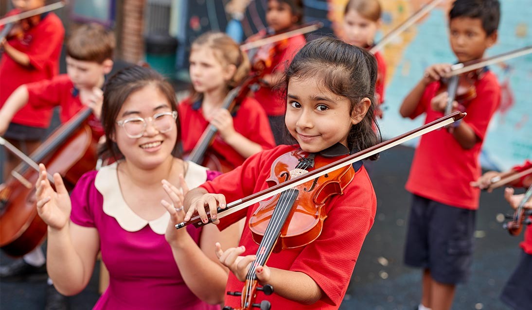 A young girl plays the violin while her teacher watches.