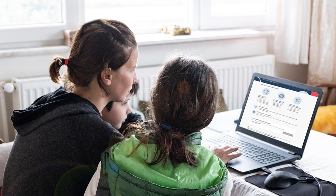 Woman and two children sit in front of a laptop with online enrolment process on the screen.