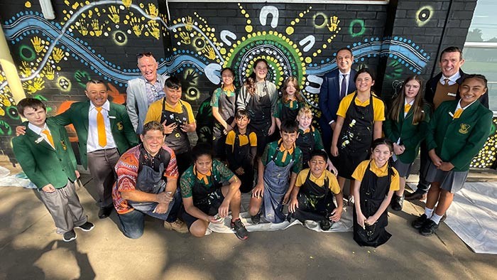 A group of people in front of an Aboriginal themed mural
