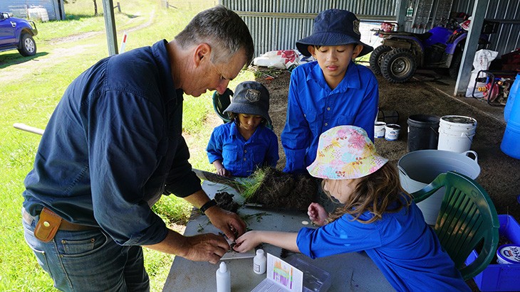 A male farmer with 3 students from Belltrees Public School in a shed testing soil samples.