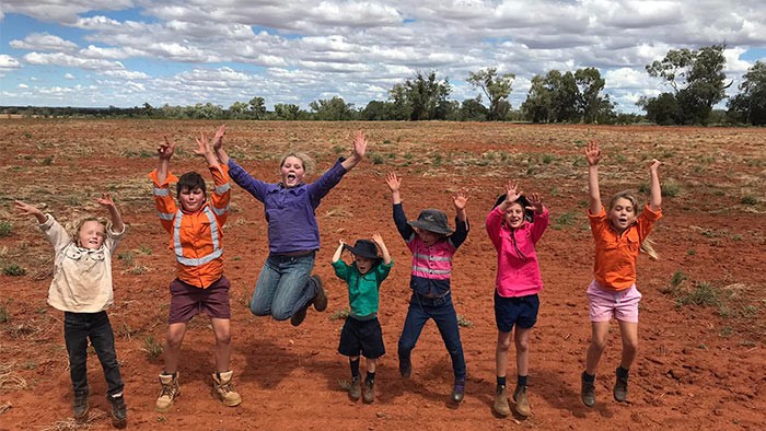 Seven students jump for joy with the backdrop a red sand paddock.